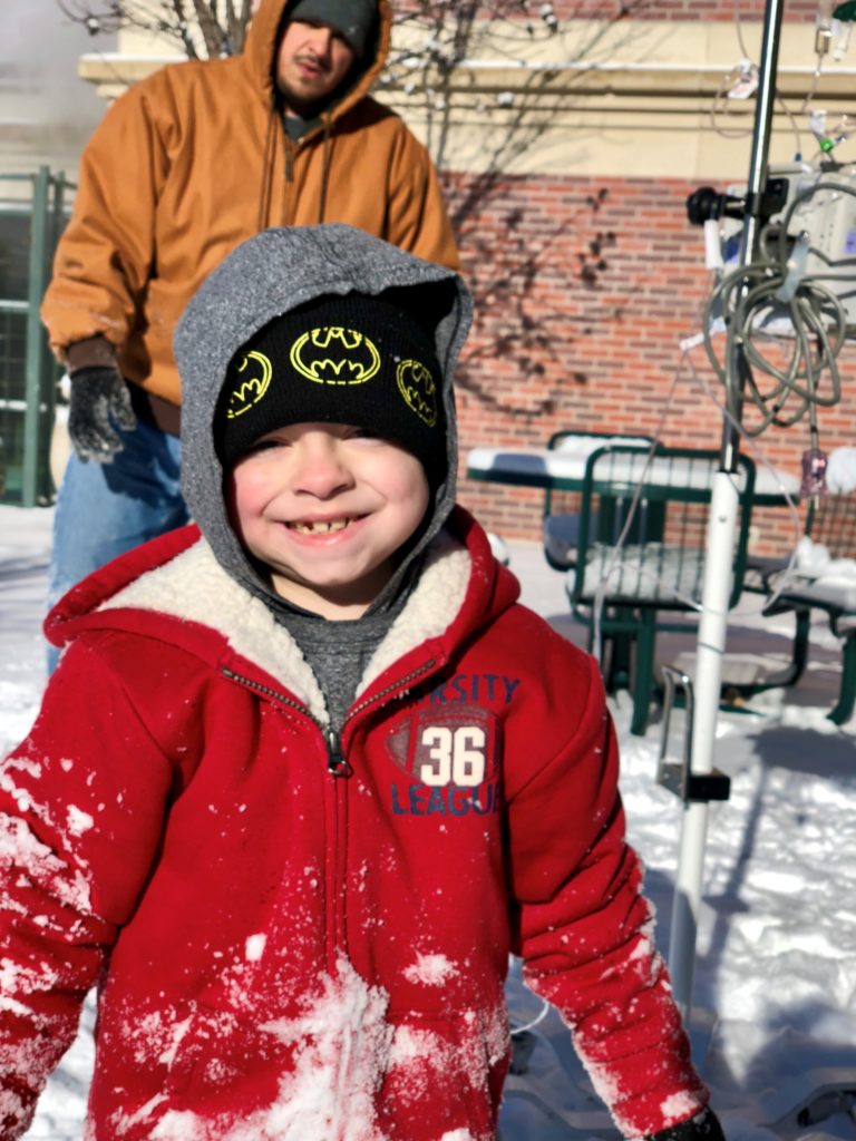 Juan standing in front of his dad, in the snow.