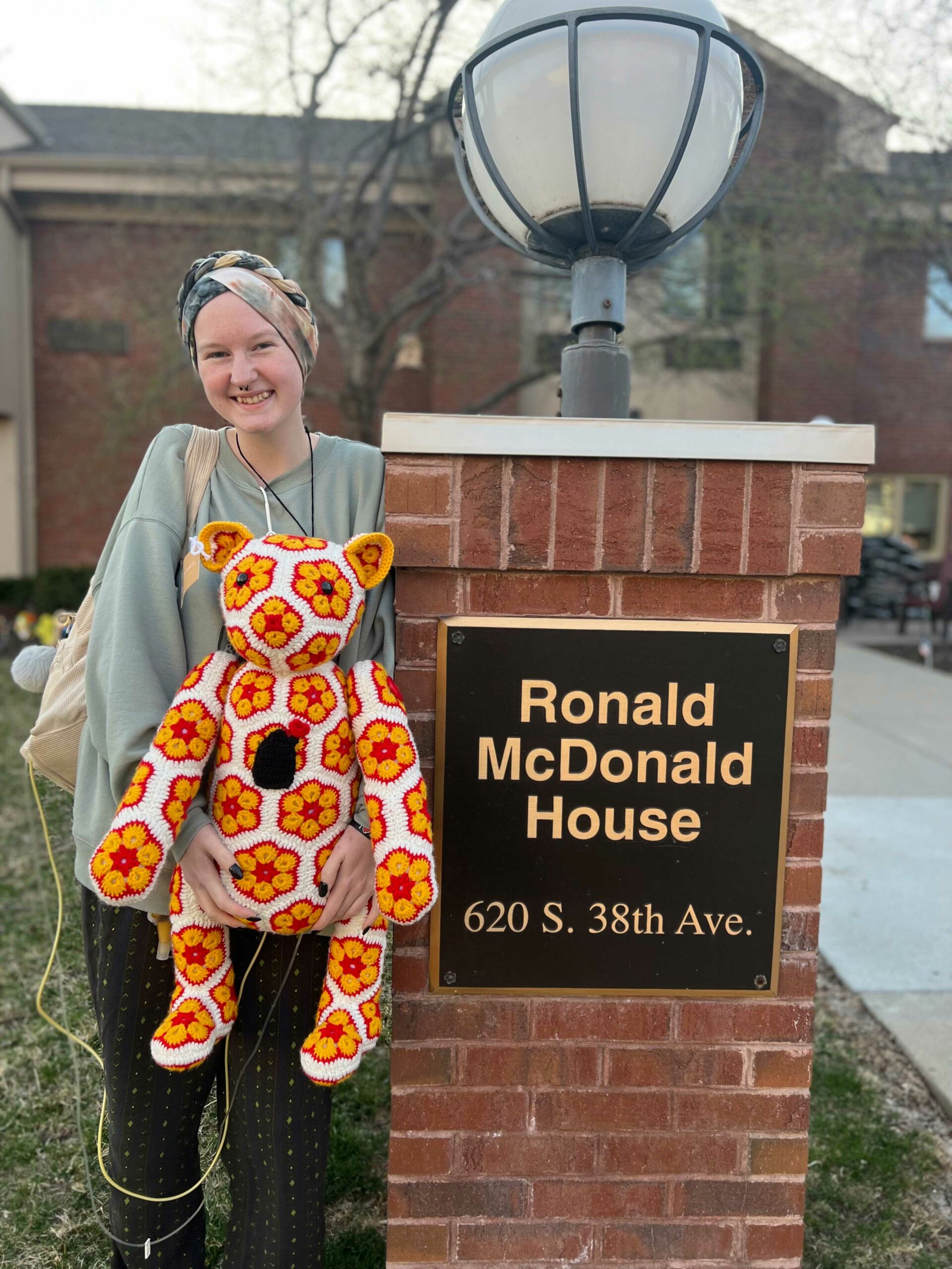 Allison Winter standing next to the Ronald McDonald House sign holding a bear she crocheted