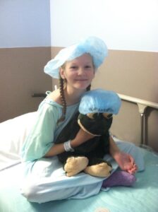 Allison in a hospital bed with a stuffed animal, preparing for surgery