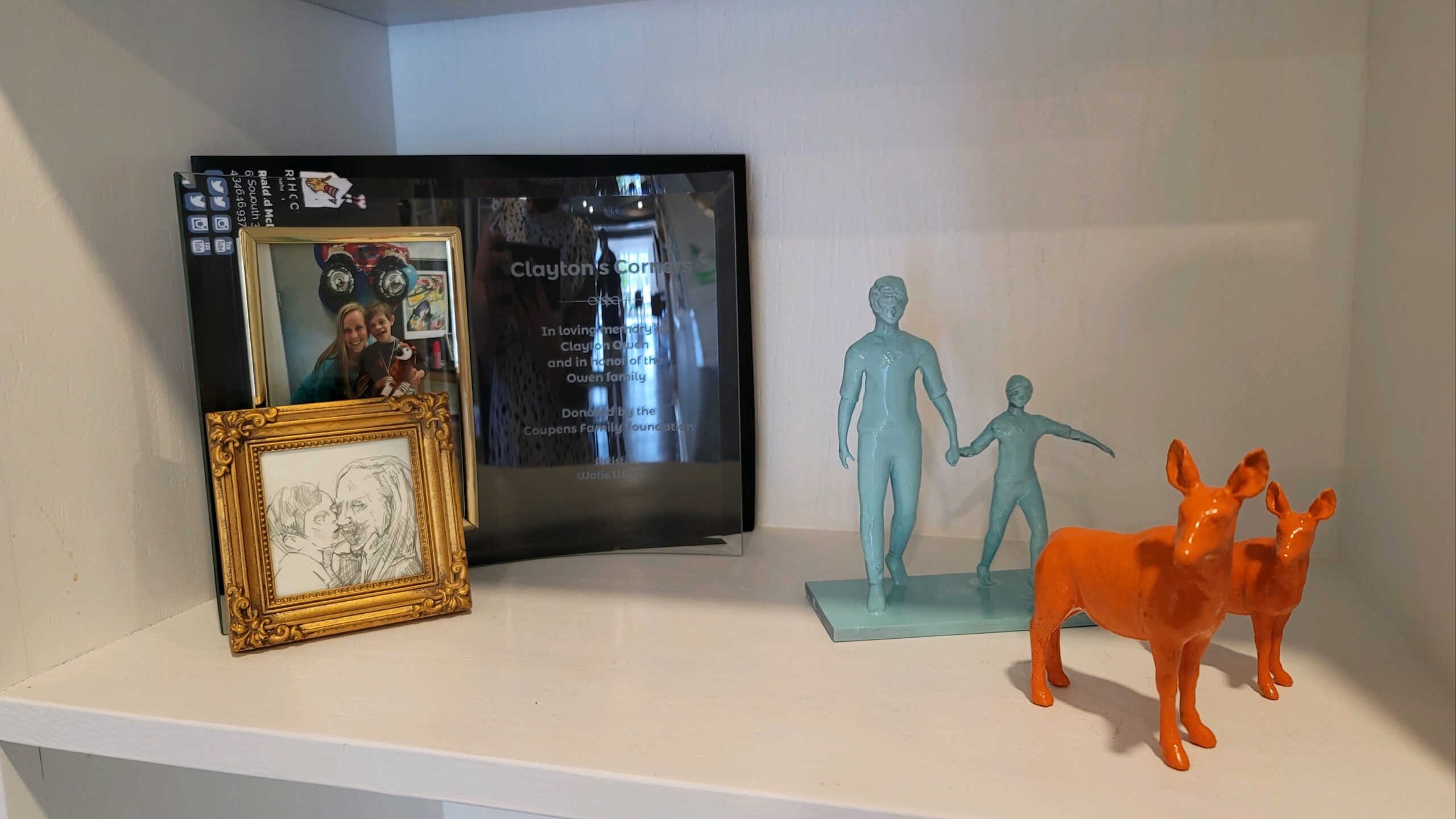 display of figurines a photo and plaque that says Clayton's Corners in loving memory of Clayton Owen and in honor of the Owen family donated by Coupens Family Foundation Artist Watie White