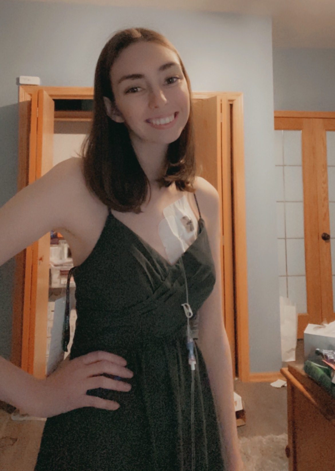 Taylor stands smiling in her room, with a main line port on her chest