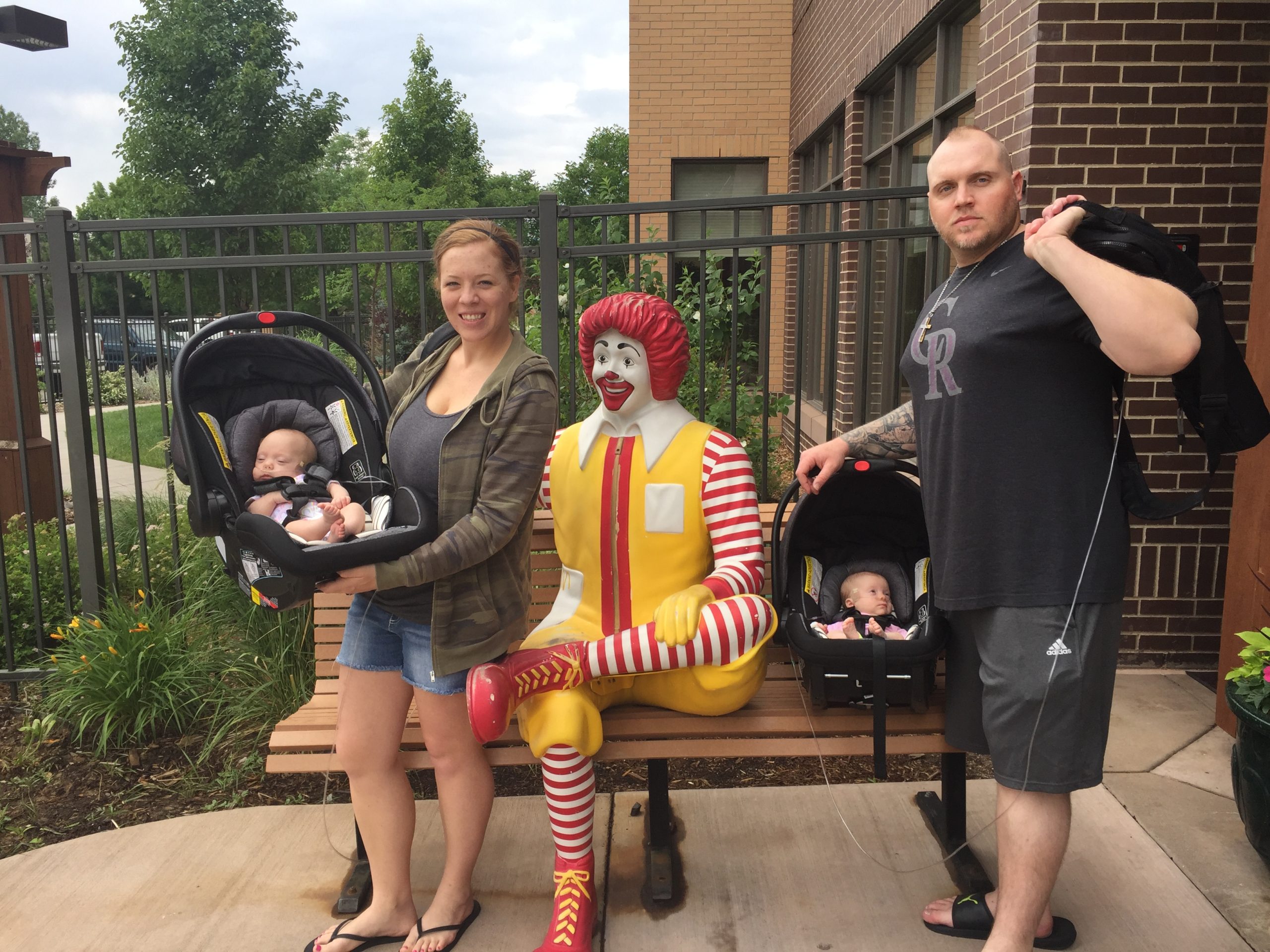Alison and Brandon pose with their newborn daughters Sawyer and Remi next to a Ronald McDonald statue