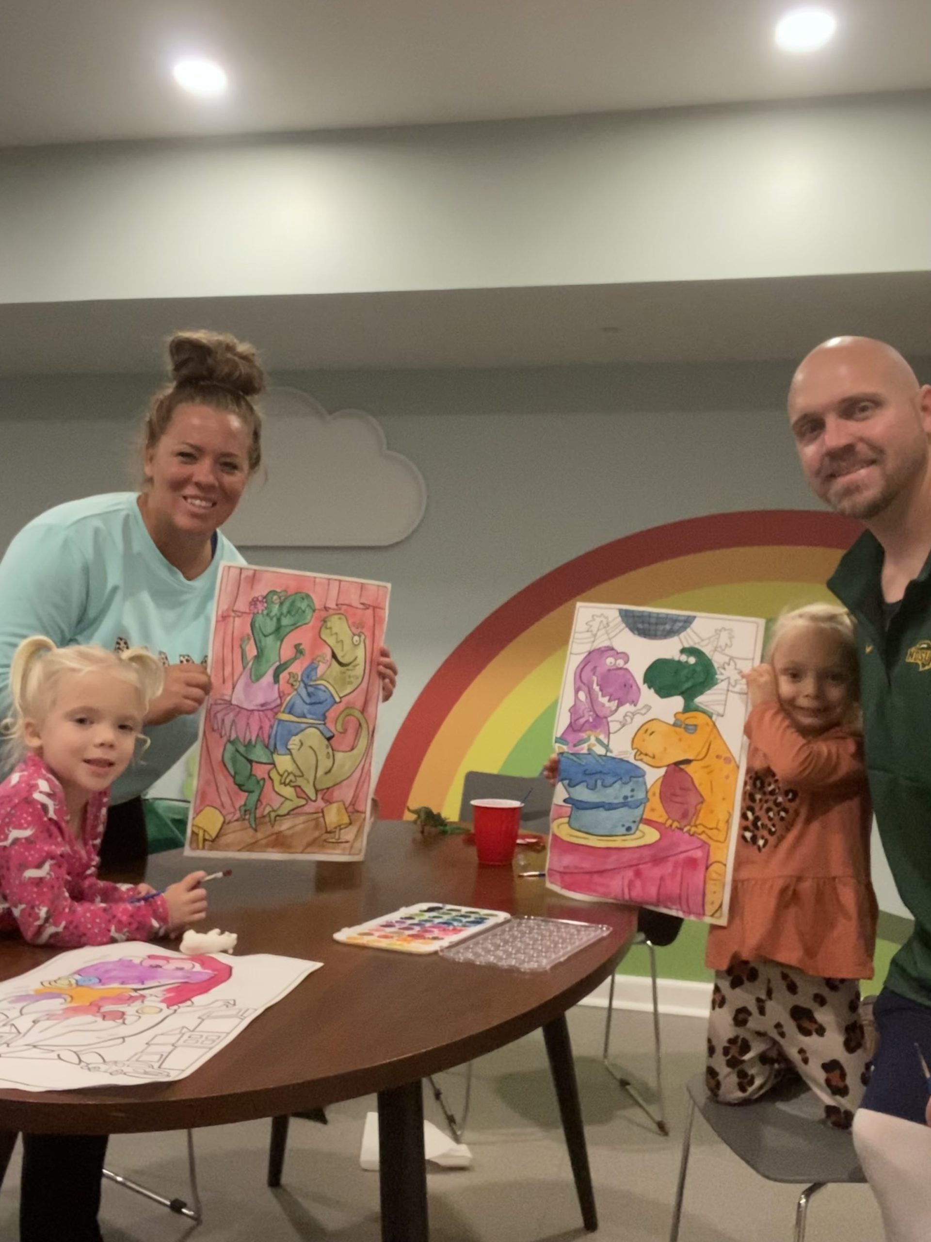Sawyer, Alison, Remi, and Brandon pose holding some paintings they created in the Ronald Mcdonald House playroom